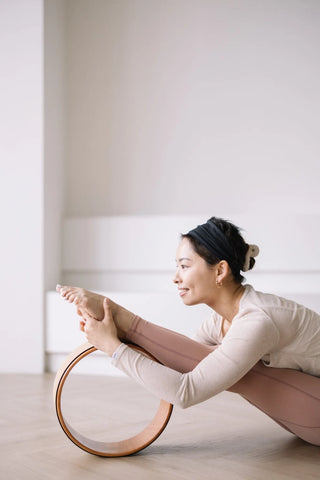 Annette Chan performing a forward bend with a wheel to enhance spinal flexibility．
